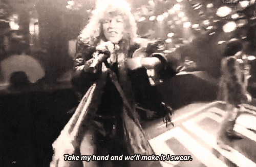 Gif from the Living On a Prayer video. Jon Bon Jovi at a mic, reaches for your hand as he sings "Take my hand and we'll make it I swear"